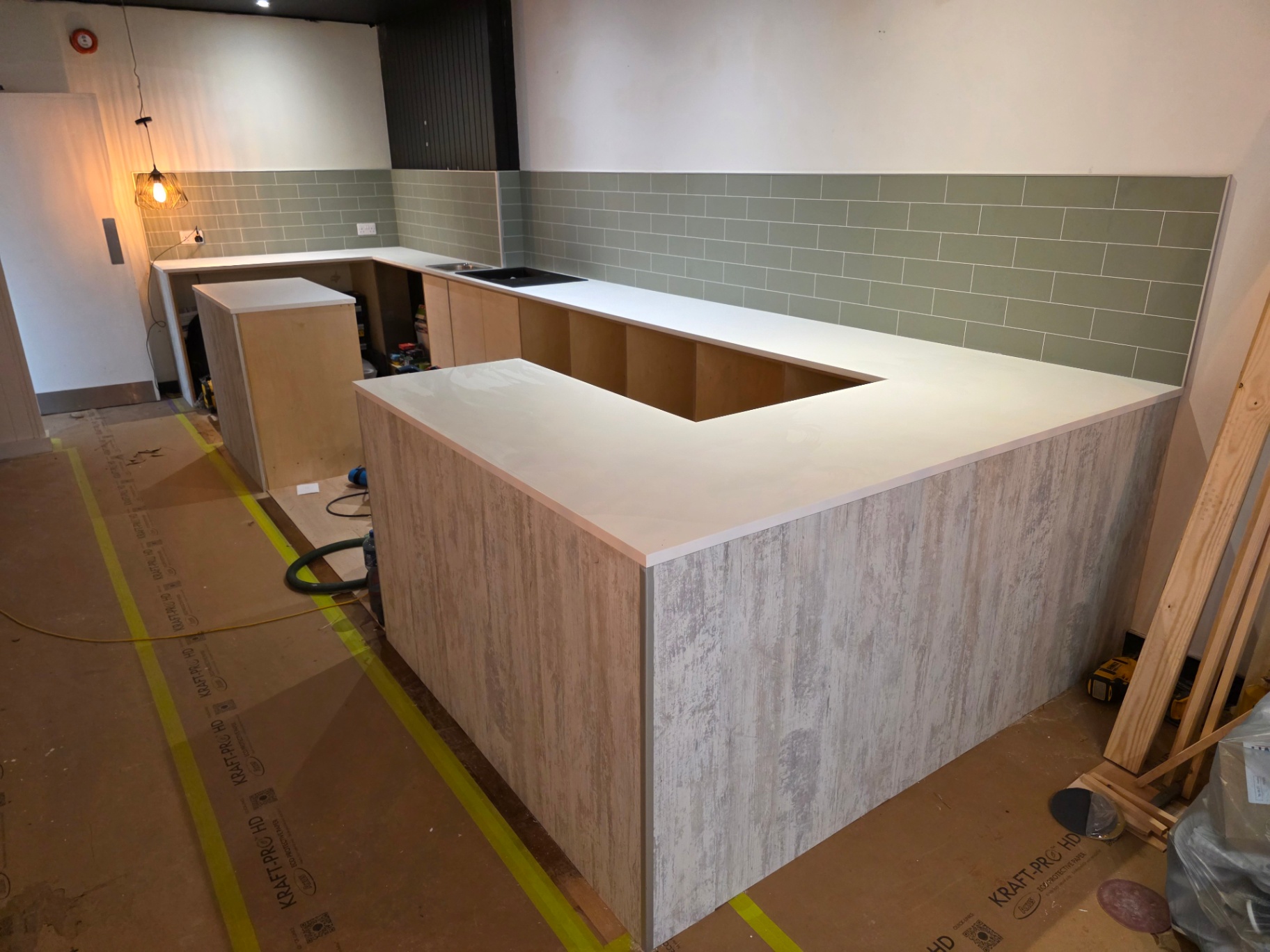 Bespoke service counter under construction with concrete-effect cladding and sage subway tiles