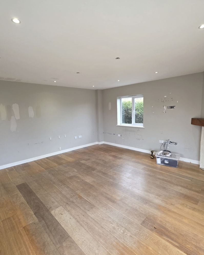 Living room before works — plain grey walls and oak flooring